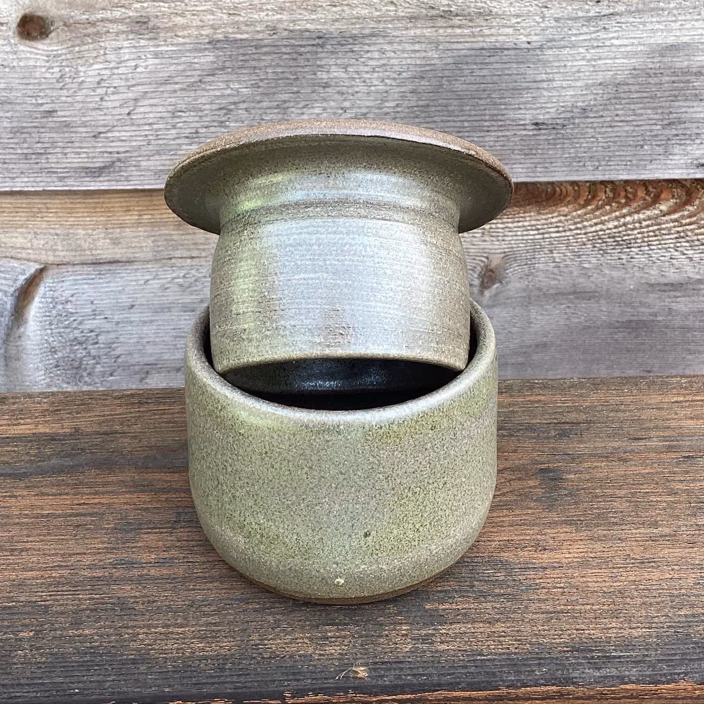 A ceramic coffee mug with a lid, placed on a wooden surface with a wooden wall in the background.
