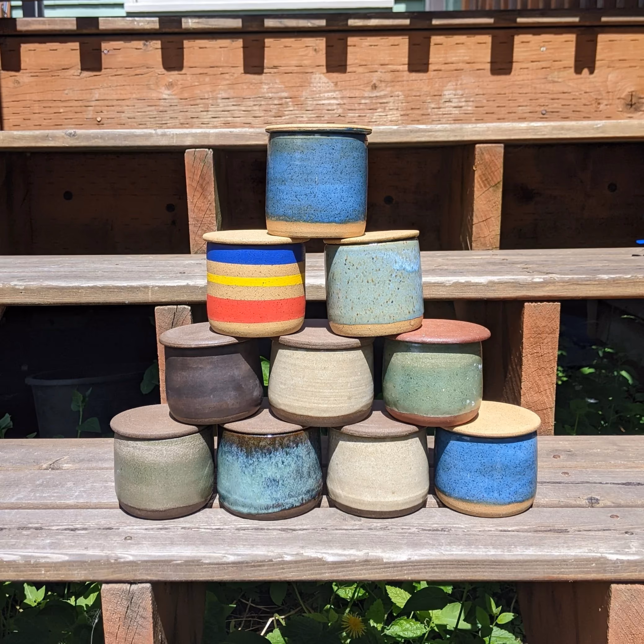 Stacked colorful ceramic pots outdoors on a wooden surface.
