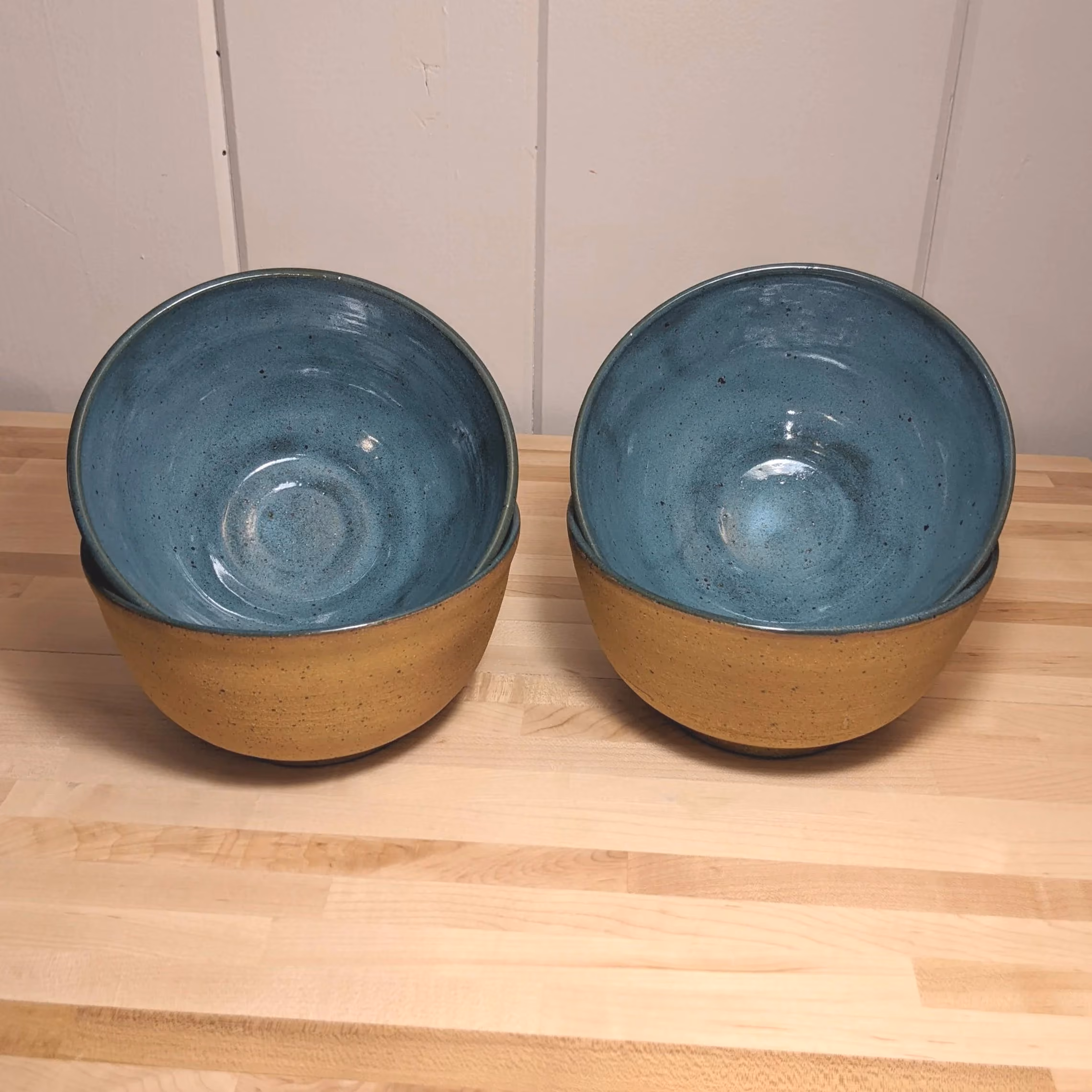 Two ceramic bowls with blue-glazed interiors and beige exteriors on a wooden surface.