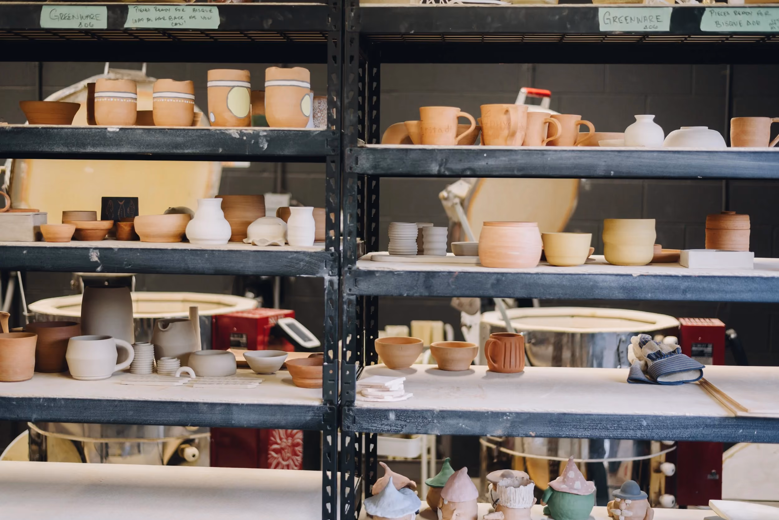 Shelves filled with unfinished pottery and ceramics in a workshop setting.
