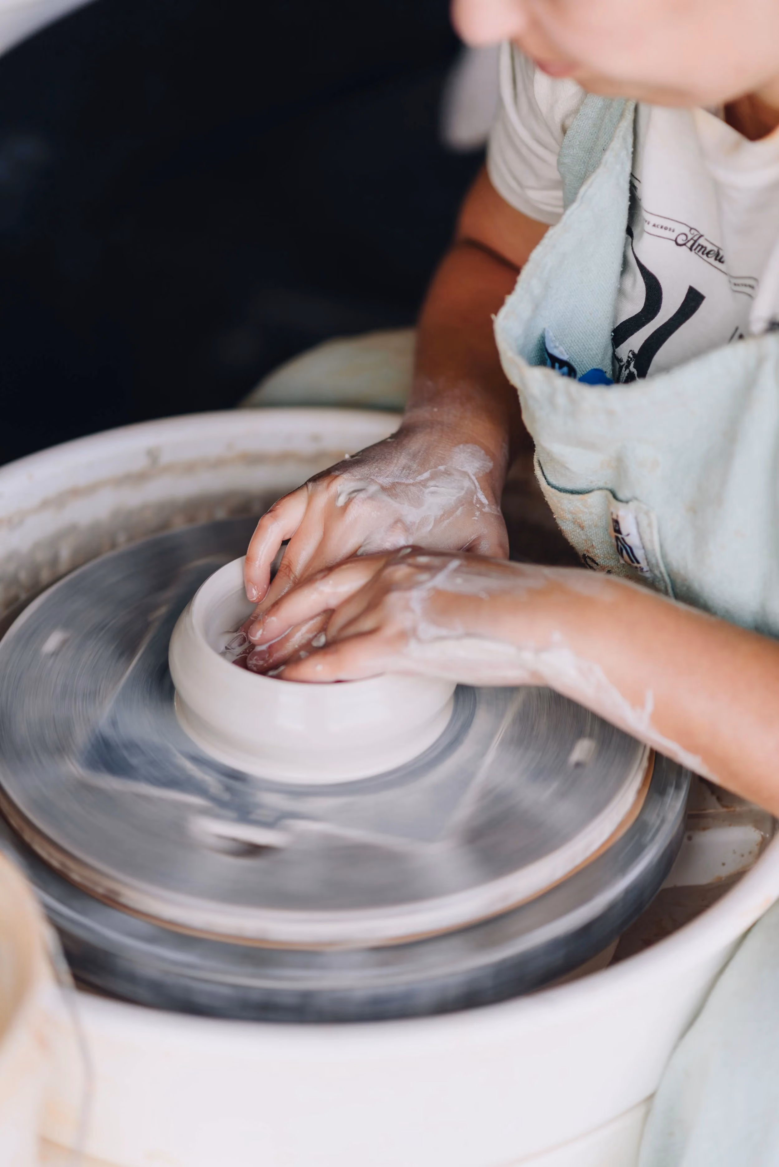 Person shaping pottery on a spinning wheel with hands covered in clay.