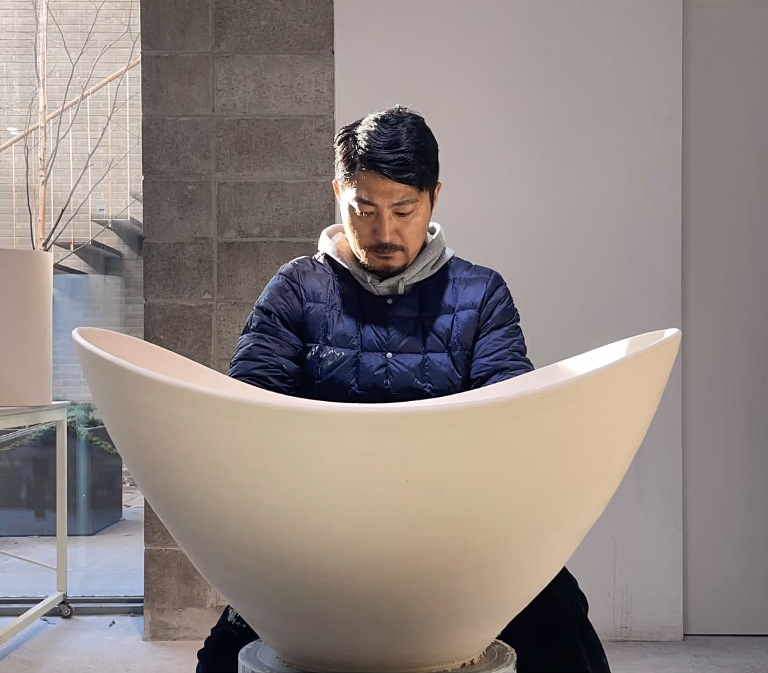 Man inspecting a large white ceramic bowl or vessel in an indoor space with a concrete wall and window.