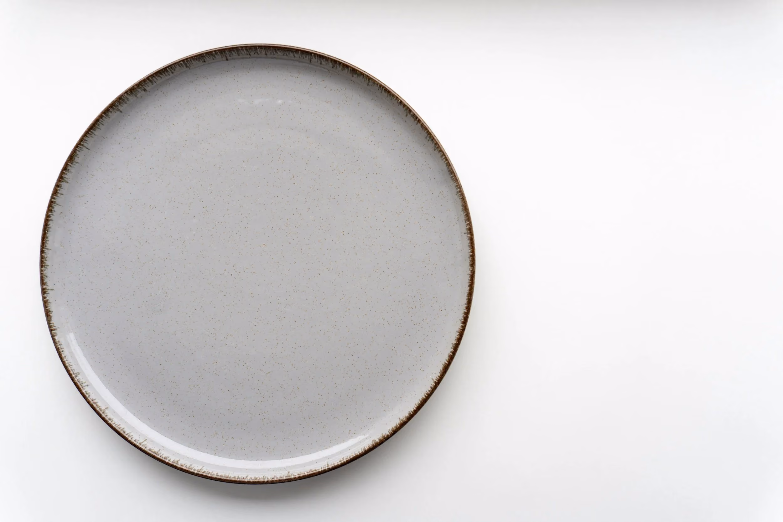 A wide ceramic plate glazed pale grey with a bare iron-brown rim, photographed from above on a white surface.